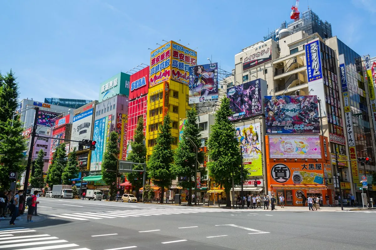 Chuo-dori in Akihabara on a sunny day, lined with colorful signs, anime billboards and street trees
