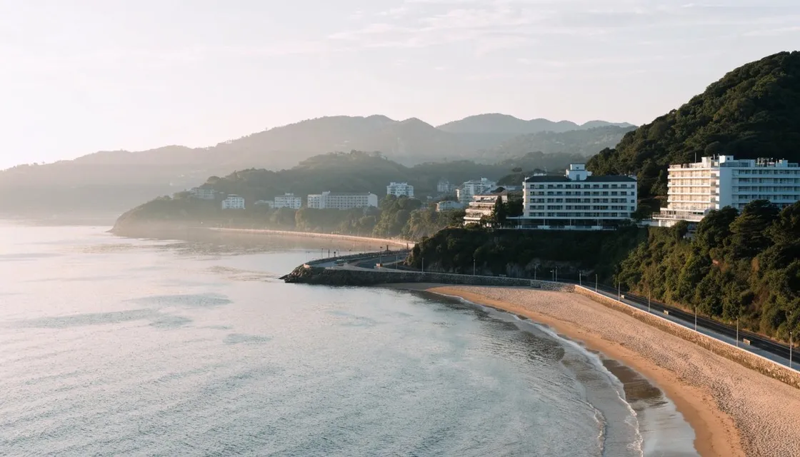 Atami bay with a curved beach, a seaside promenade and hotels climbing the hillside in soft morning light