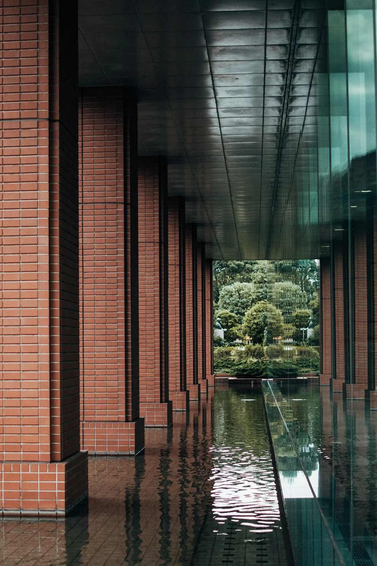 A quiet brick colonnade beside a shallow water channel in Ebisu, opening onto green trees