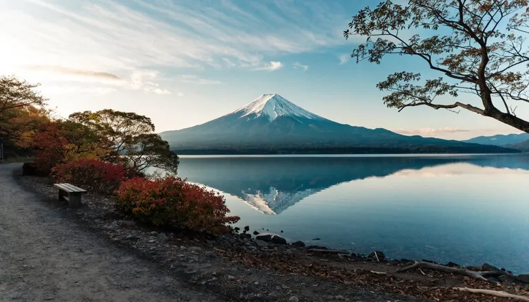 Mount Fuji reflected in a calm lake at dawn, with a wooden bench and autumn foliage along the shore