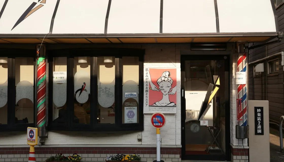 A neighborhood barbershop in Japan with striped barber poles beside the door