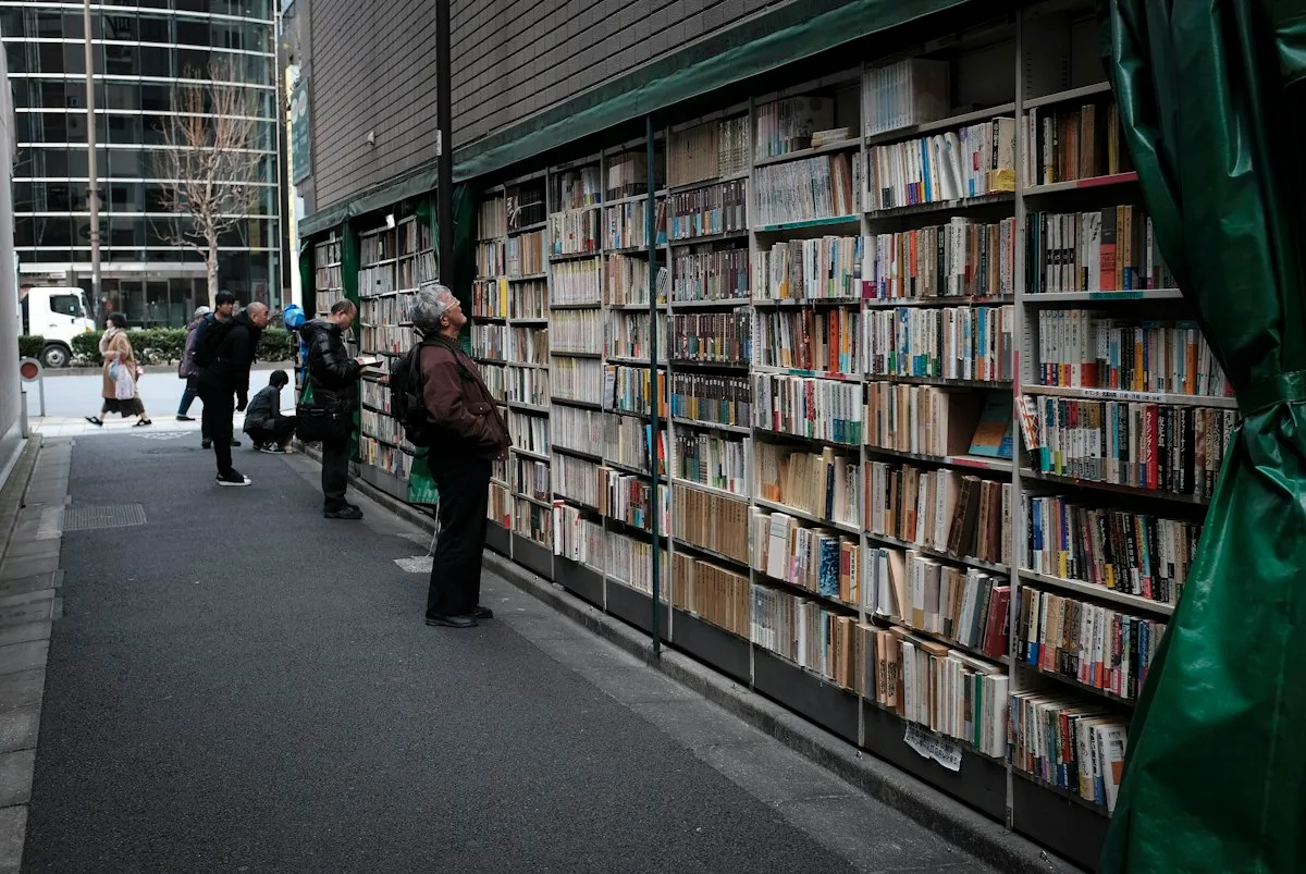 People browsing tall outdoor bookshelves on a side street in Jimbocho