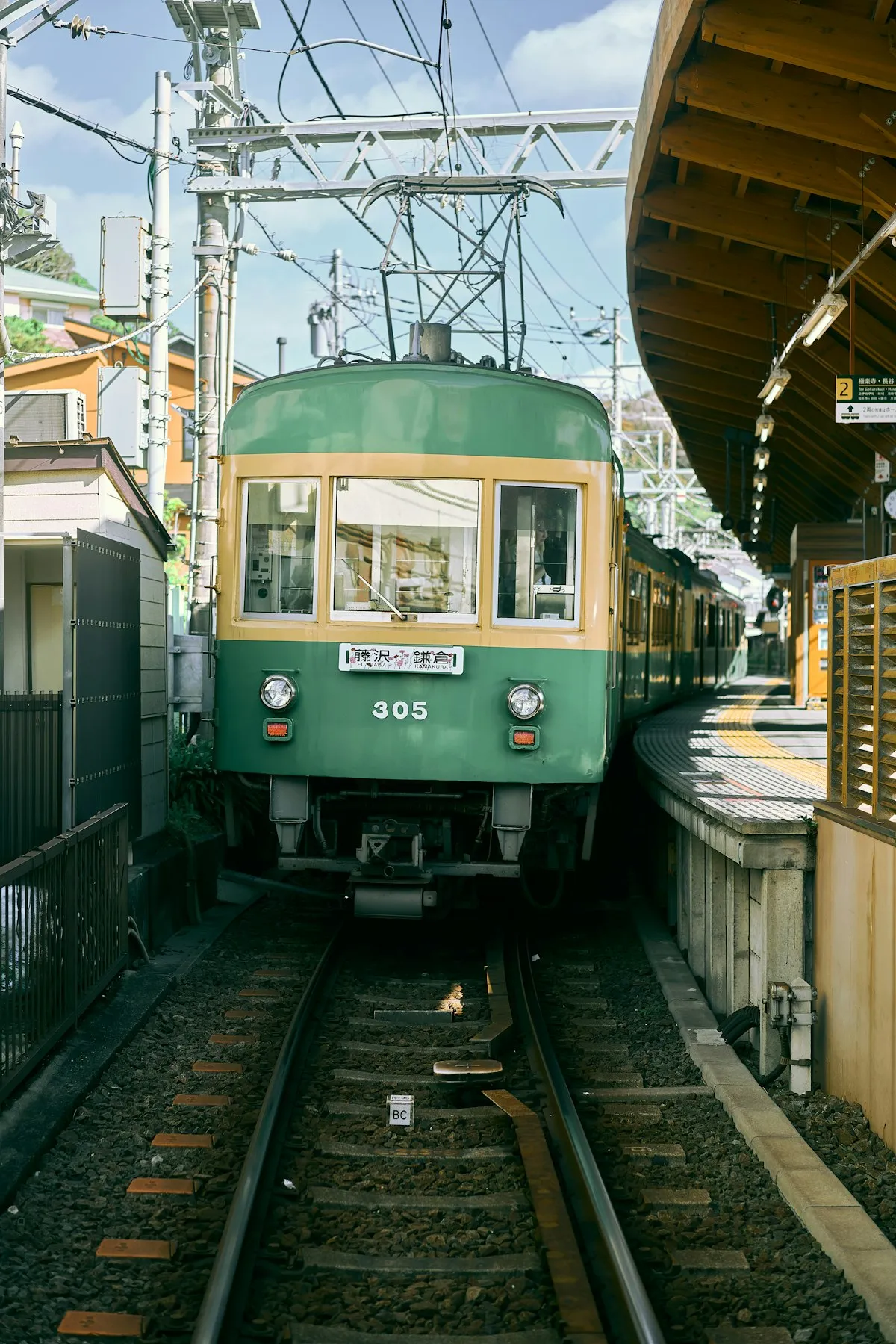 A green-and-cream Enoden train pulling into a small station, its destination board reading Fujisawa and Kamakura
