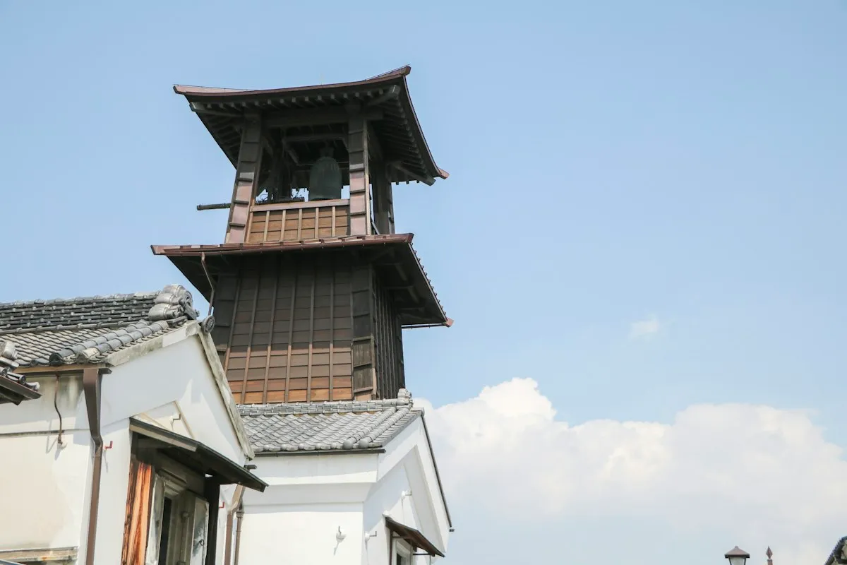 白壁の建物の上にそびえる、川越の木造の鐘楼「時の鐘」