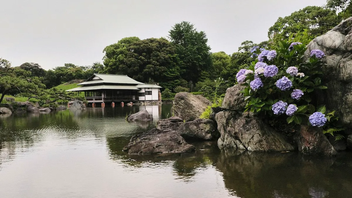 The pond at Kiyosumi Garden with large rocks, blue hydrangeas and a wooden teahouse over the water