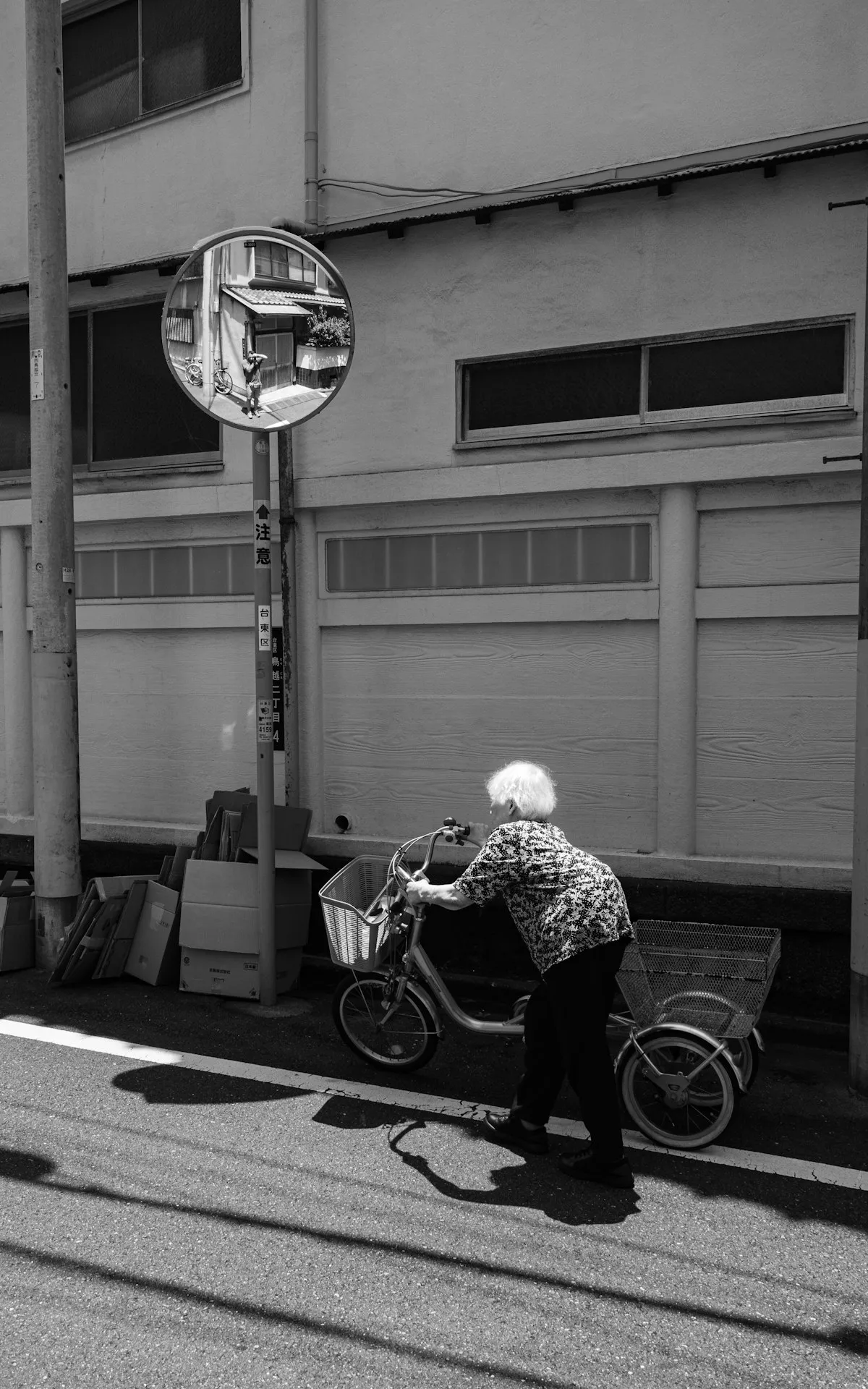 蔵前の静かな通りで自転車を押す年配の女性（モノクロ写真）