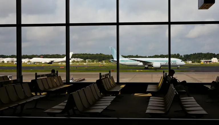 An airport departure gate with rows of seats and a plane outside the window