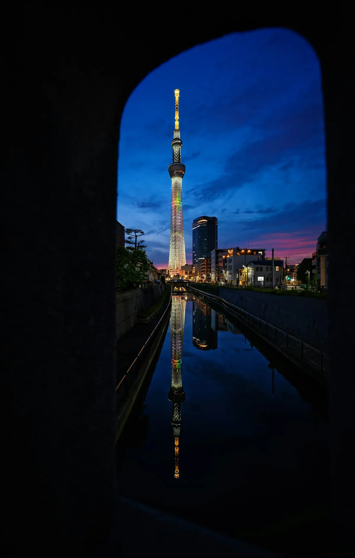 Tokyo Skytree lit up at dusk and reflected in the still canal water in Oshiage