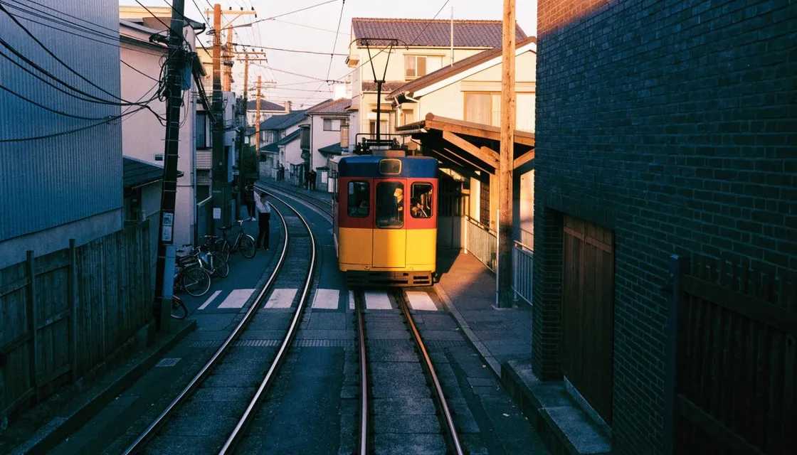 A colorful two-car Setagaya Line tram approaching a narrow level crossing in Sangenjaya at golden hour