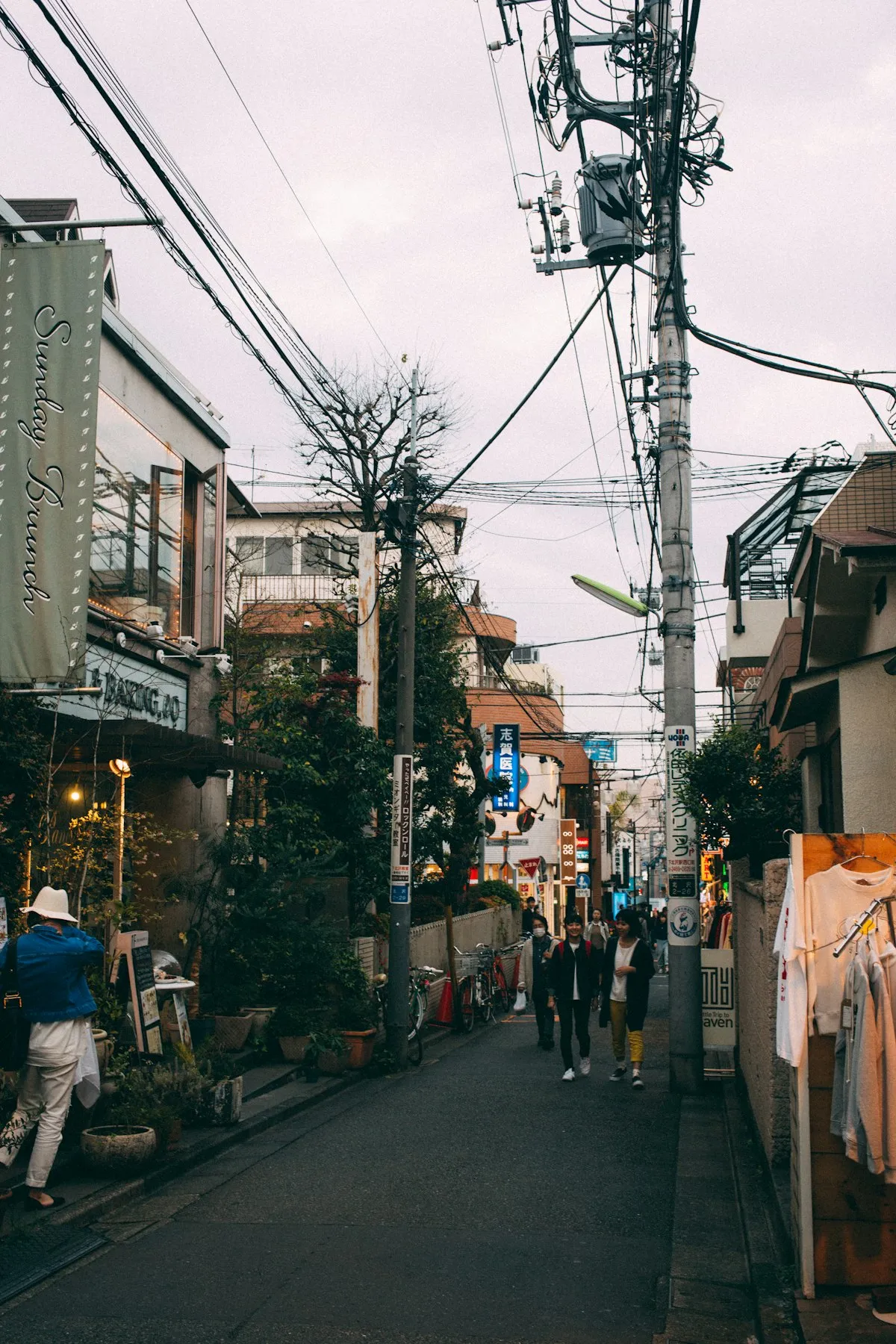 A narrow Shimokitazawa street with small shops, potted plants and overhead power lines