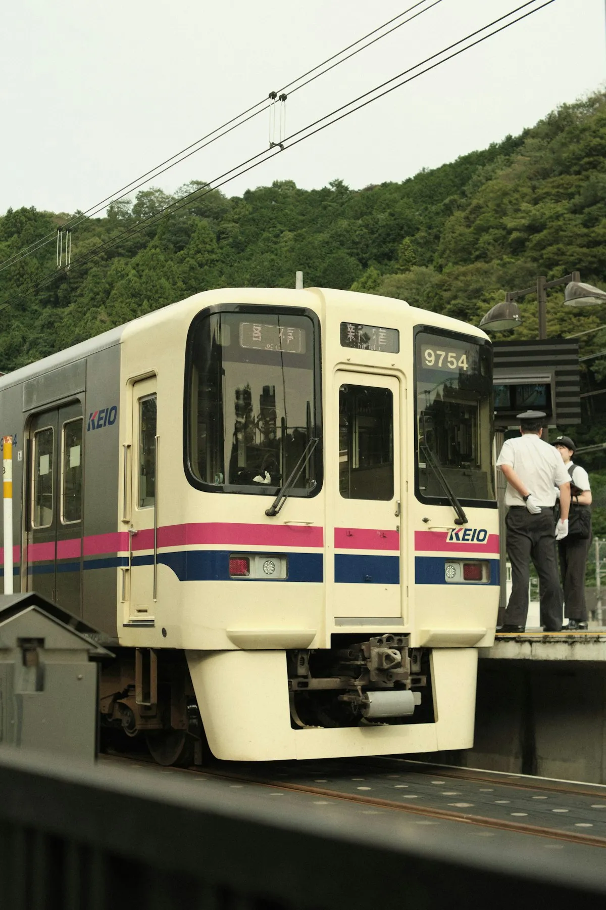 A Keio line train at Takaosanguchi Station, with green hills behind