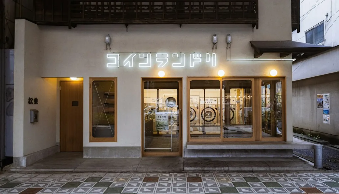 A modern coin laundry storefront with a lit sign and washing machines inside