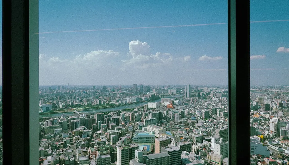 A tall hotel window looking out over Tokyo's neighborhoods under a blue sky