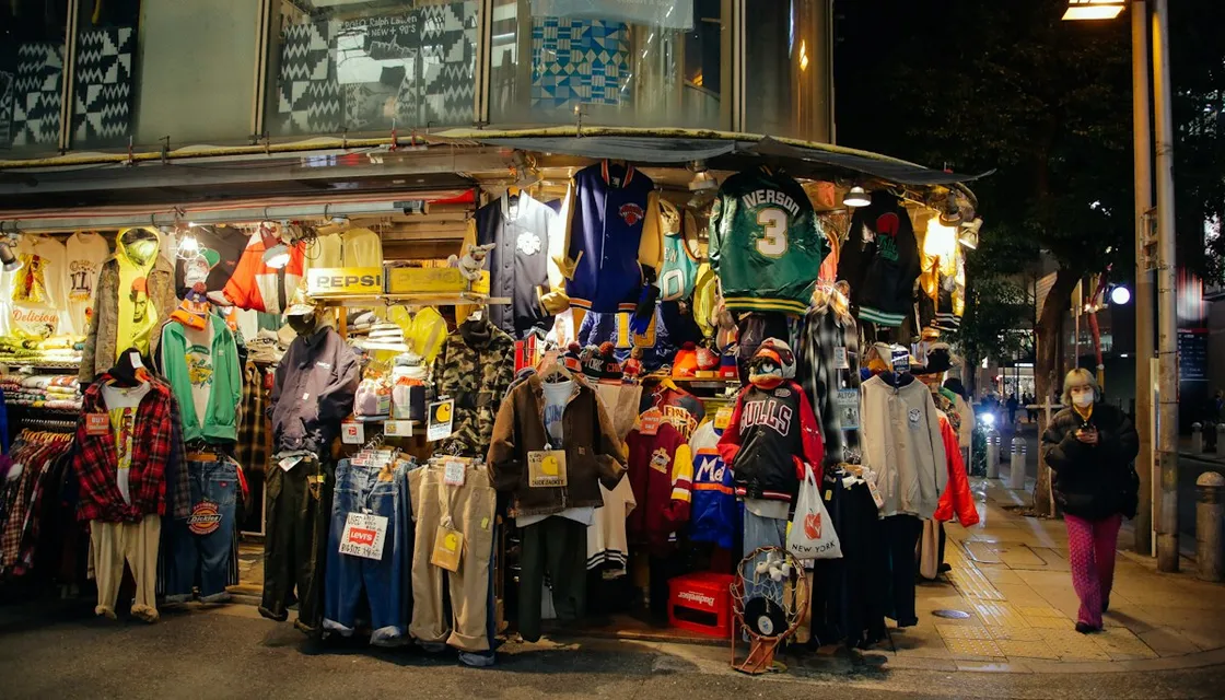 Racks of used jackets and sweaters outside a secondhand clothing shop at night