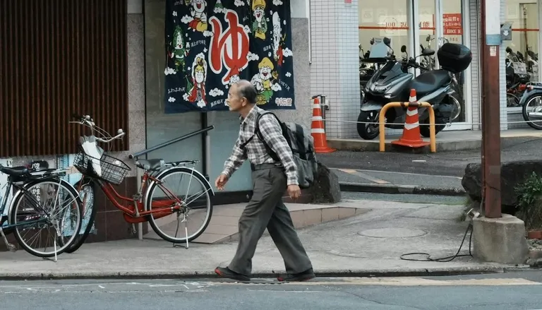 「ゆ」ののれんが掛かる街の銭湯の前を歩く男性と、停められた自転車