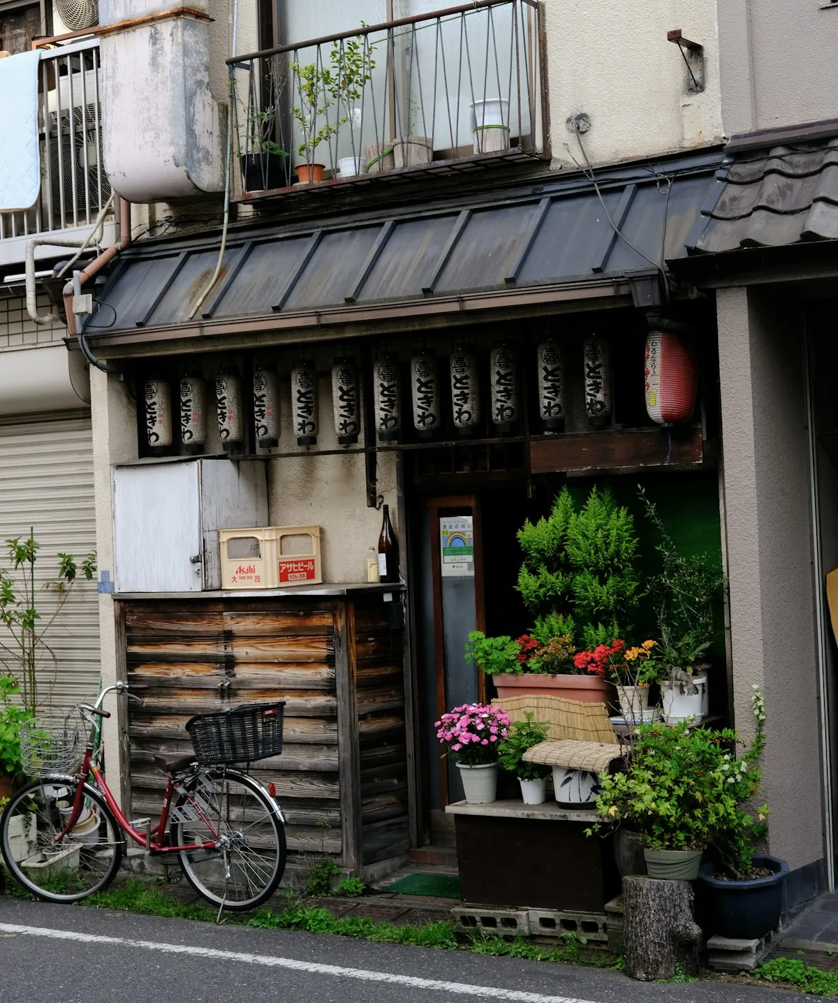 ちょうちんが下がる谷中の古い2階建て。店先に鉢植えの花と自転車